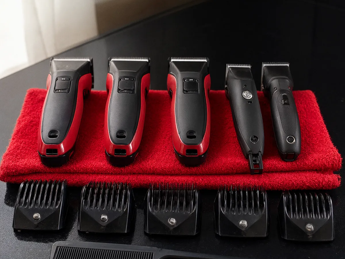 Red and black clippers and trimmers on a folded red towel with black guards and a comb