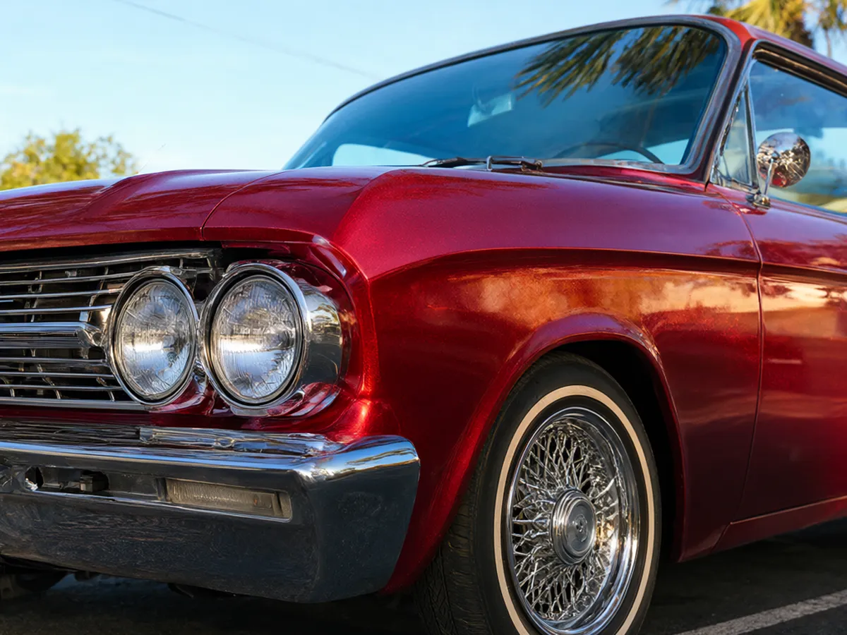 The front of a candy-red lowrider with chrome wire wheels and a white-wall tire in the sun